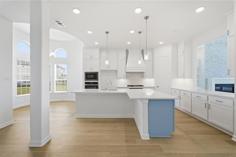 Contemporary kitchen featuring a large central island with a contrasting accent panel, white cabinetry, integrated stainless steel appliances, and sleek pendant lighting