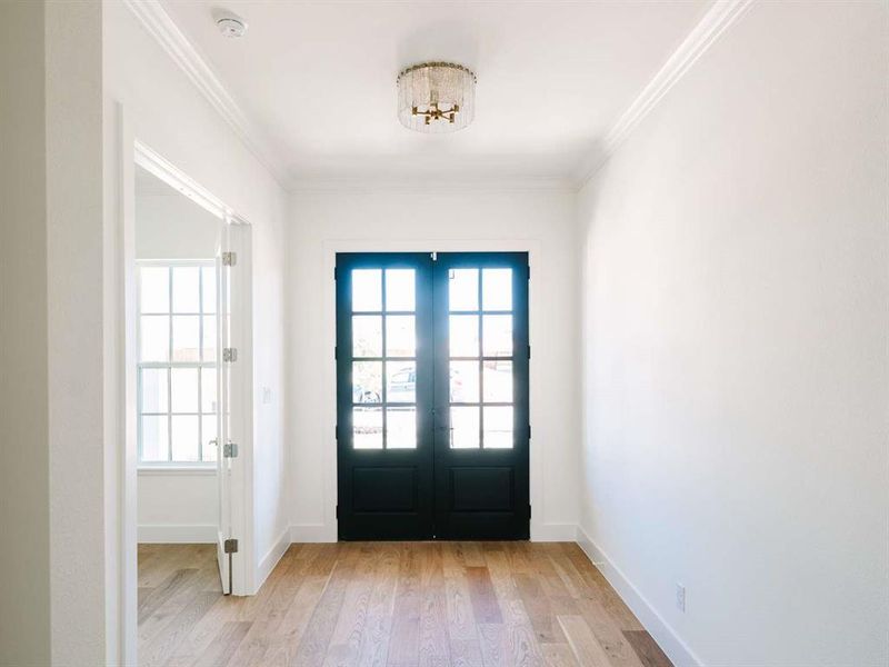 Foyer featuring french doors, crown molding, light hardwood / wood-style floors, and a chandelier