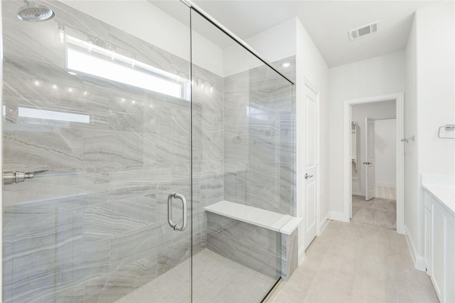 Walk-in shower with glass door, marble tile walls, built-in bench, and rain showerhead in a white bathroom