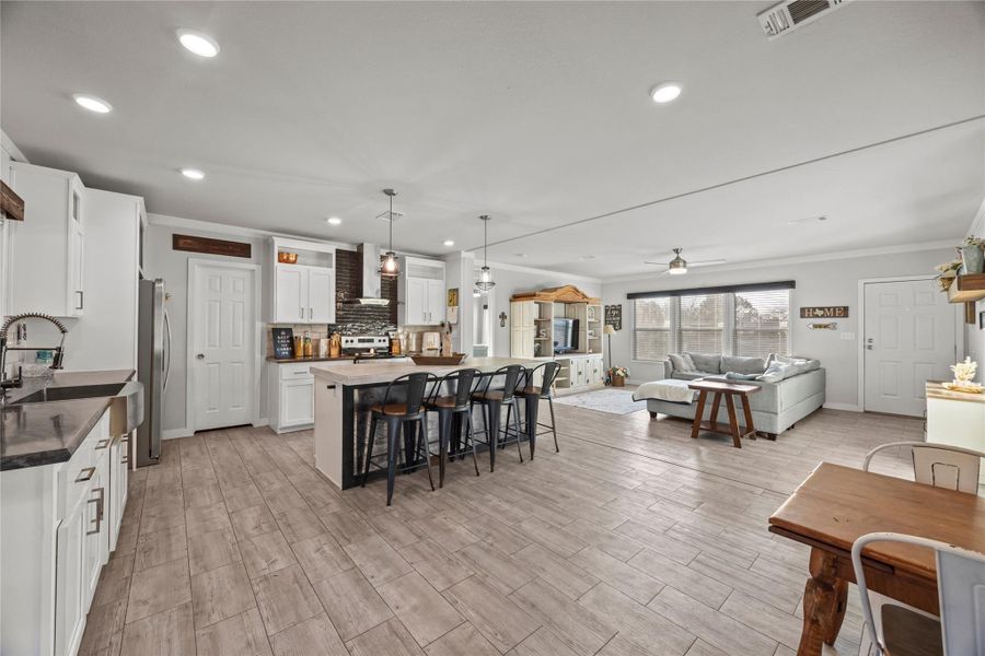 Kitchen with open floor plan, white cabinetry, ornamental molding, hanging light fixtures, and a breakfast bar