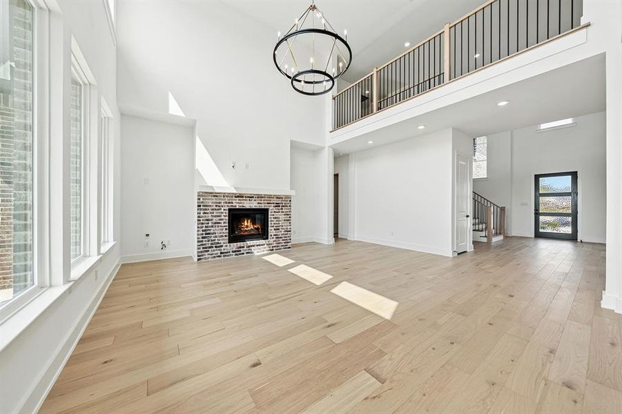 Unfurnished living room featuring a glass covered fireplace, a high ceiling, stairs, light wood-type flooring, and a chandelier