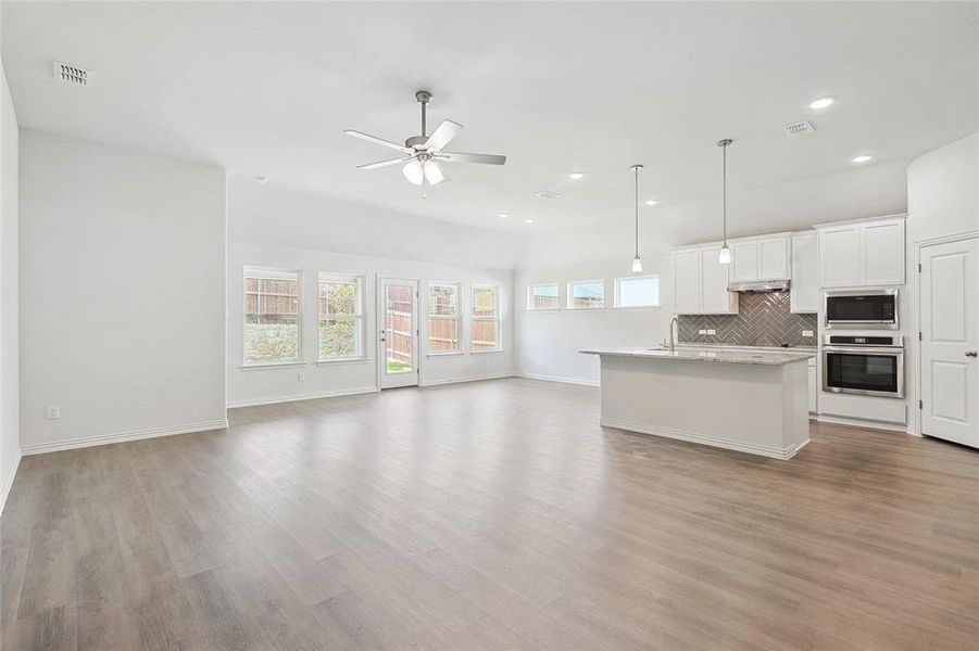 Kitchen with white cabinetry, backsplash, a kitchen island with sink, light hardwood / wood-style floors, and appliances with stainless steel finishes