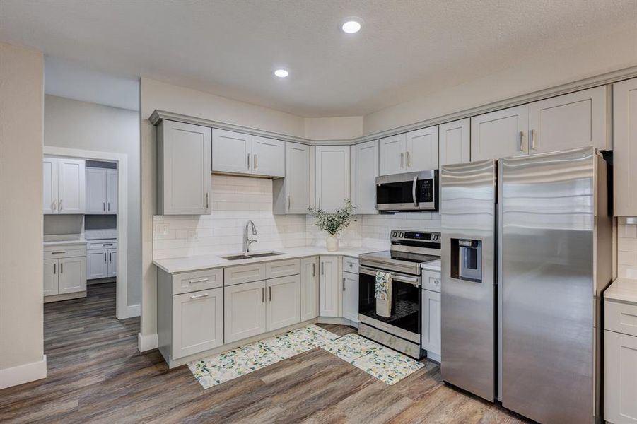 Kitchen featuring backsplash, appliances with stainless steel finishes, wood-type flooring, sink, and gray cabinetry