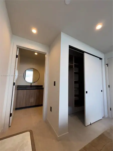 Built-in closet with sliding doors and custom shelving, vanity featuring a rectangular vessel sink and wood-finish cabinetry, circular wall-mounted mirror, and recessed ceiling lighting Built-in closet with sliding doors and custom shelving, vanity featuring a rectangular vessel sink and wood-finish cabinetry, circular wall-mounted mirror, and recessed ceiling lighting