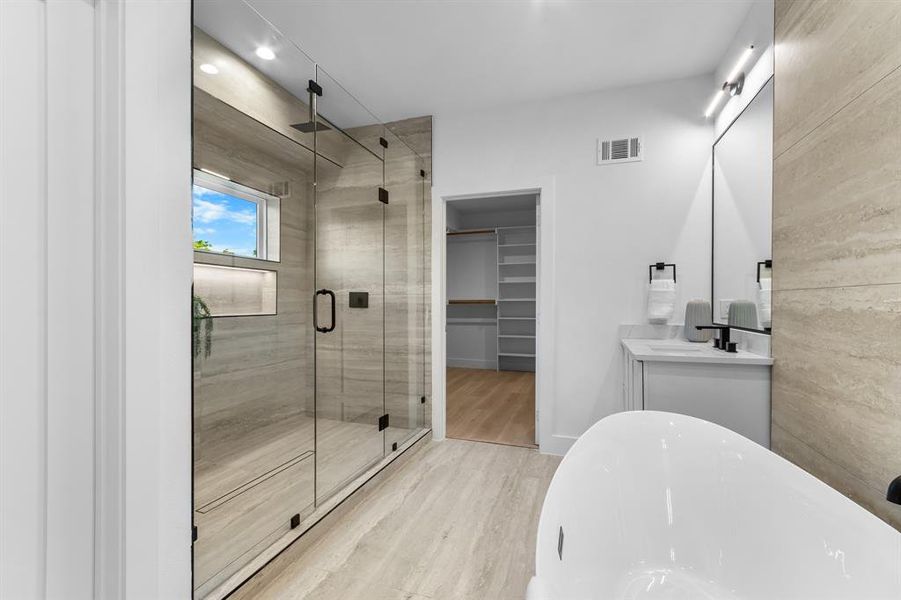 Spacious bathroom featuring a glass-enclosed shower with stone-look tile, integrated shelving, and a window Spacious bathroom featuring a glass-enclosed shower with stone-look tile, integrated shelving, and a window