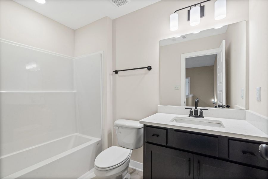 Bathroom featuring a white tub/shower combination, dark wood-finish vanity with a white countertop, undermount sink, matte black faucet, and a large wall-mounted mirror Bathroom featuring a white tub/shower combination, dark wood-finish vanity with a white countertop, undermount sink, matte black faucet, and a large wall-mounted mirror