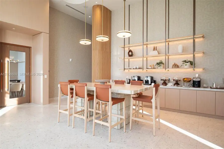 High-ceilinged room featuring a stone-clad island, custom built-in floating shelves with integrated lighting, flat-panel cabinetry, and multi-tier pendant lighting