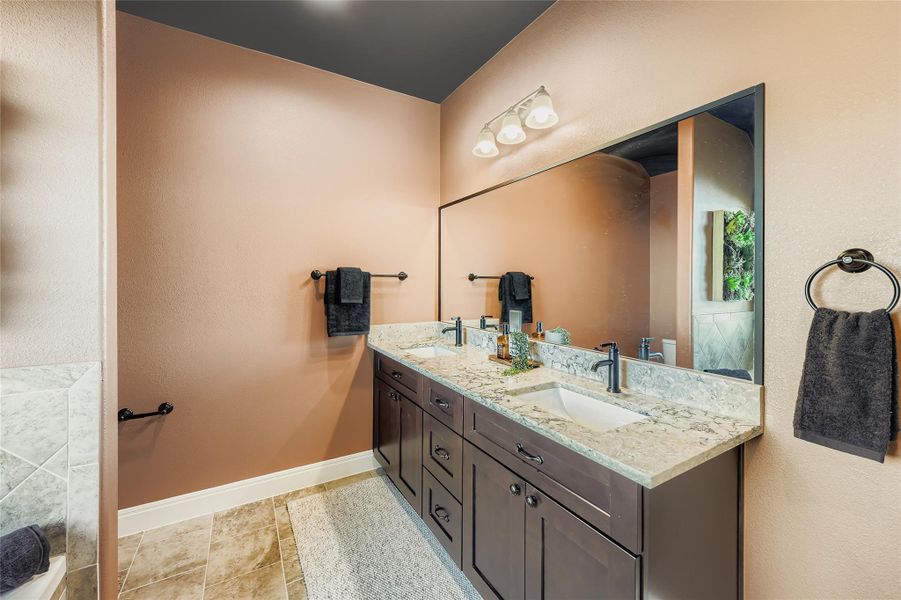 Bathroom featuring double vanity, a textured wall, and light tile patterned floors