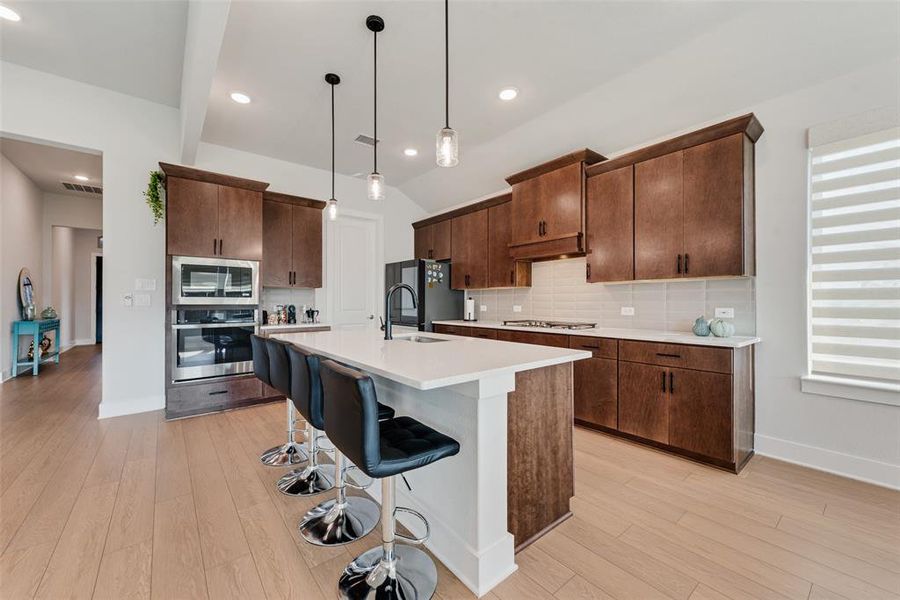 Kitchen featuring decorative backsplash, pendant lighting, a breakfast bar, dark brown cabinetry, and lofted ceiling