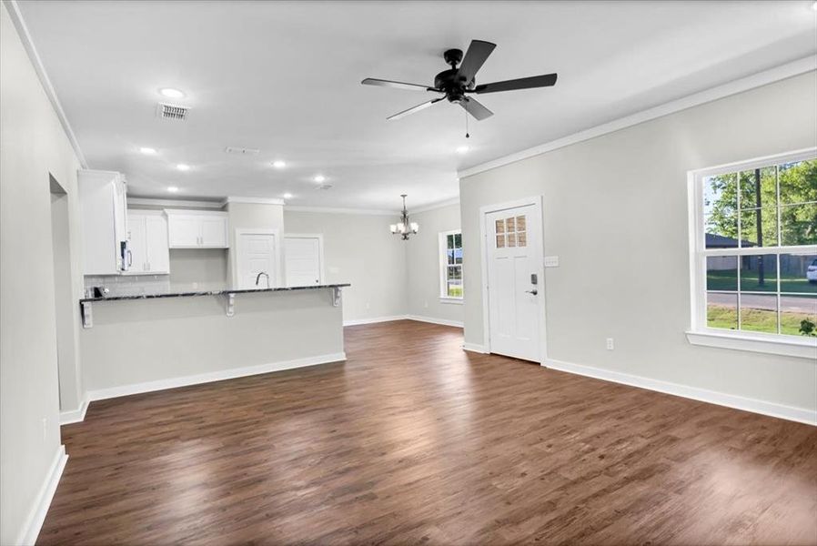 Unfurnished living room with a chandelier, ornamental molding, healthy amount of natural light, a ceiling fan, and dark wood finished floors