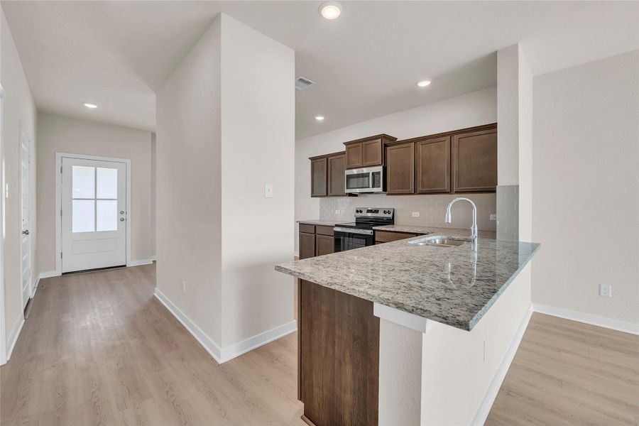 Kitchen with tasteful backsplash, appliances with stainless steel finishes, light stone countertops, dark brown cabinets, and a peninsula