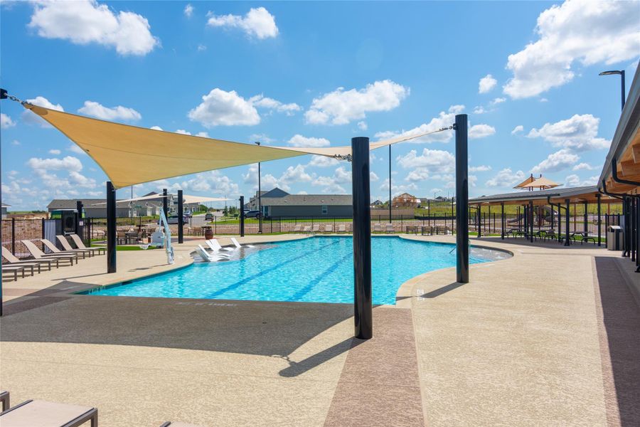 Expansive outdoor swimming pool featuring a curved design, sunshade sails, a wide concrete deck, and a covered pavilion structure