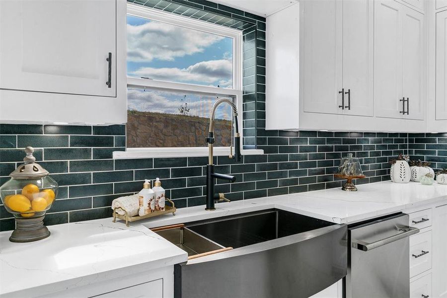 Kitchen with backsplash, sink, stainless steel dishwasher, white cabinetry, and light stone counters