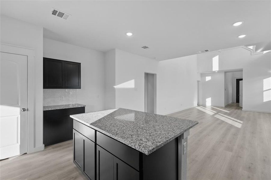 Kitchen with dark cabinets, light wood-type flooring, light stone countertops, a center island, and recessed lighting