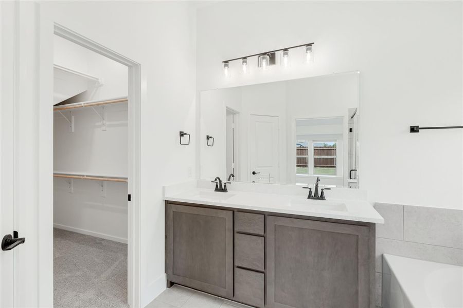 Bathroom with double sink vanity, gray cabinets, white countertop, and walk-in closet visible through open door Bathroom with double sink vanity, gray cabinets, white countertop, and walk-in closet visible through open door