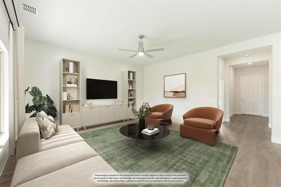 Living room with hardwood floors, ceiling fan, built-in shelving, and two orange accent chairs around a round coffee table Living room with hardwood floors, ceiling fan, built-in shelving, and two orange accent chairs around a round coffee table