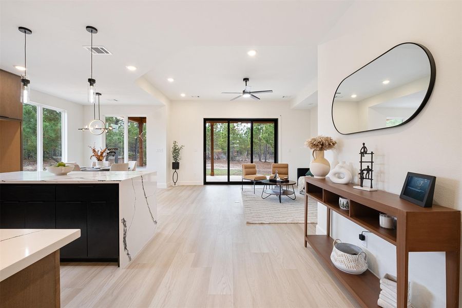 Kitchen featuring dark cabinets, decorative light fixtures, light wood-style flooring, light stone counters, and open floor plan