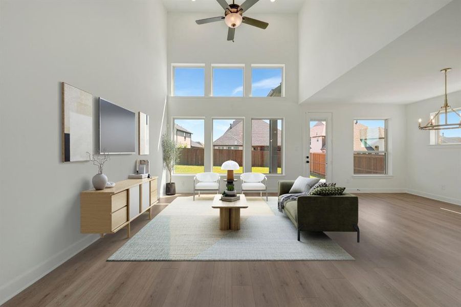 Two-story living area featuring a vaulted ceiling with a ceiling fan, wood-finish flooring, a series of upper and lower windows, and a built-in chandelier
