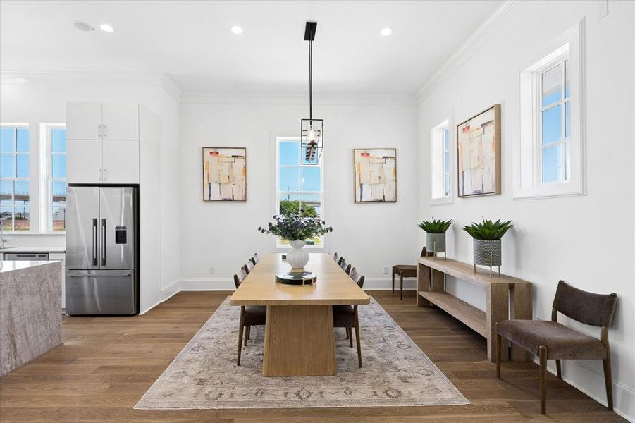 Open-concept dining area featuring wood-finish flooring, white walls, and crown molding