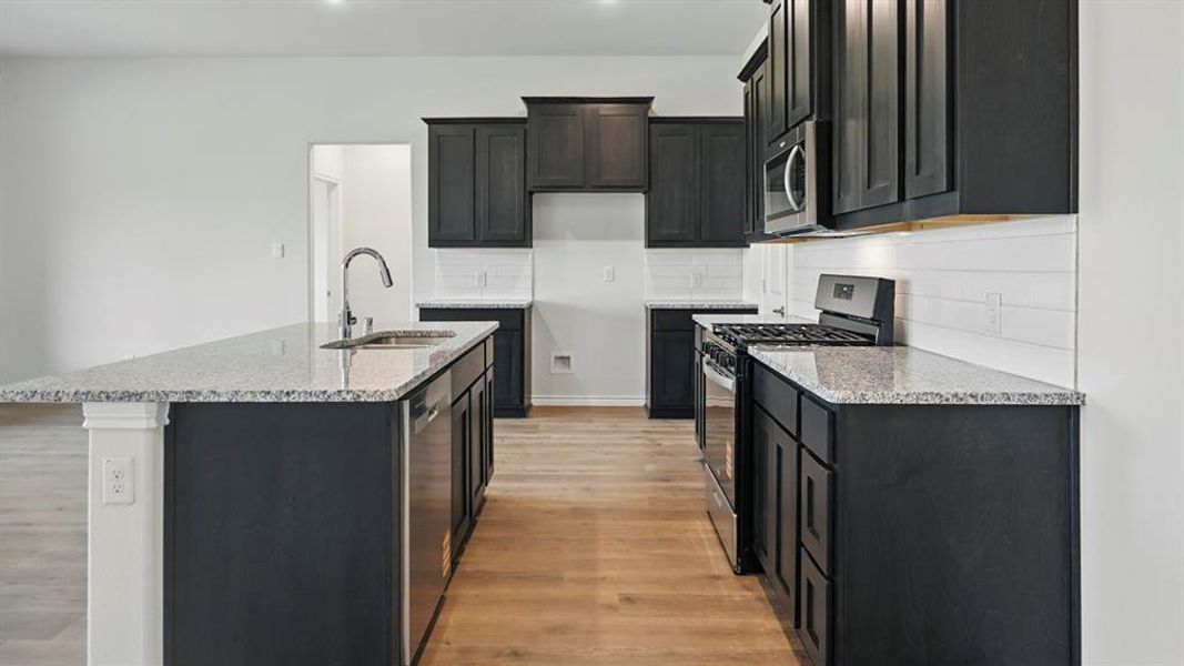 Kitchen with stainless steel appliances, light stone counters, light wood finished floors, a center island with sink, and recessed lighting