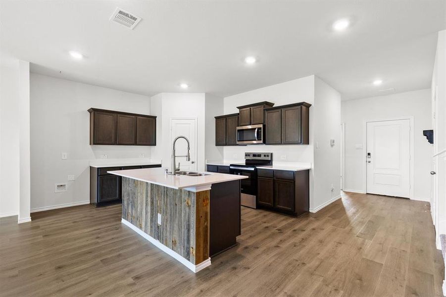 Open-concept kitchen featuring an island with wood-finish paneling, dark wood cabinetry, stainless steel appliances, white countertops, and wood-look flooring