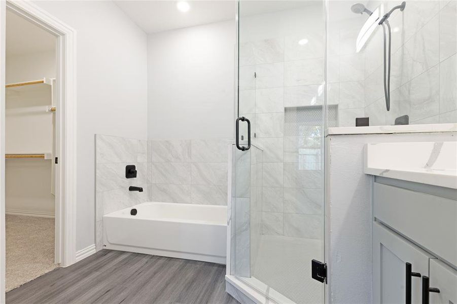 Full bath featuring vanity, a walk in closet, a stall shower, wood finished floors, and a garden tub