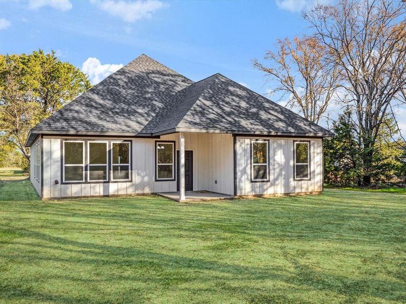 View of front of property featuring roof with shingles, a patio area, a front yard, and board and batten siding