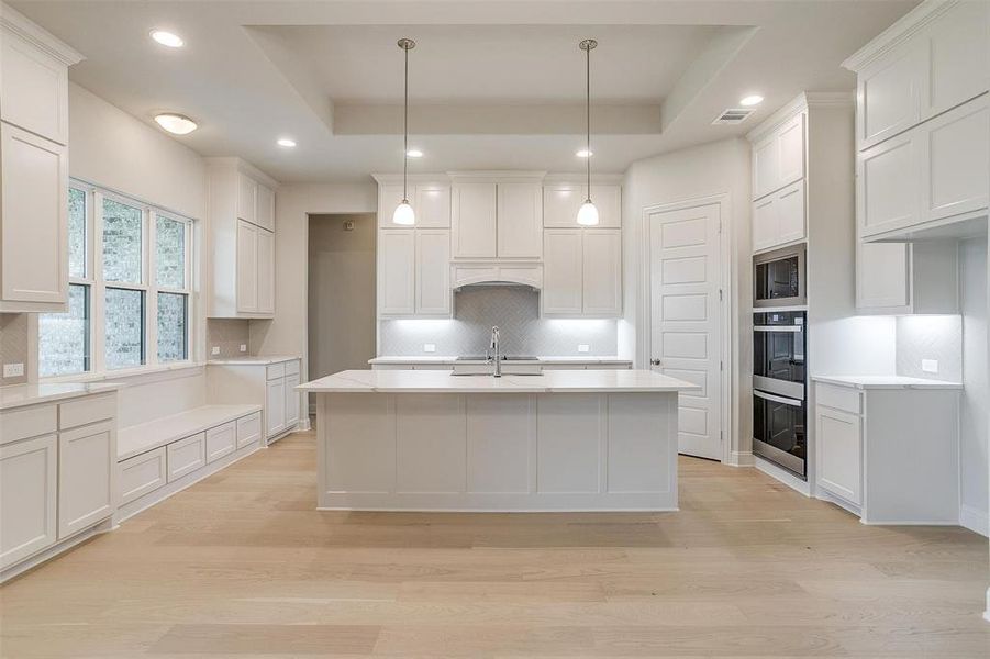 Kitchen with decorative backsplash, light hardwood / wood-style flooring, and a tray ceiling