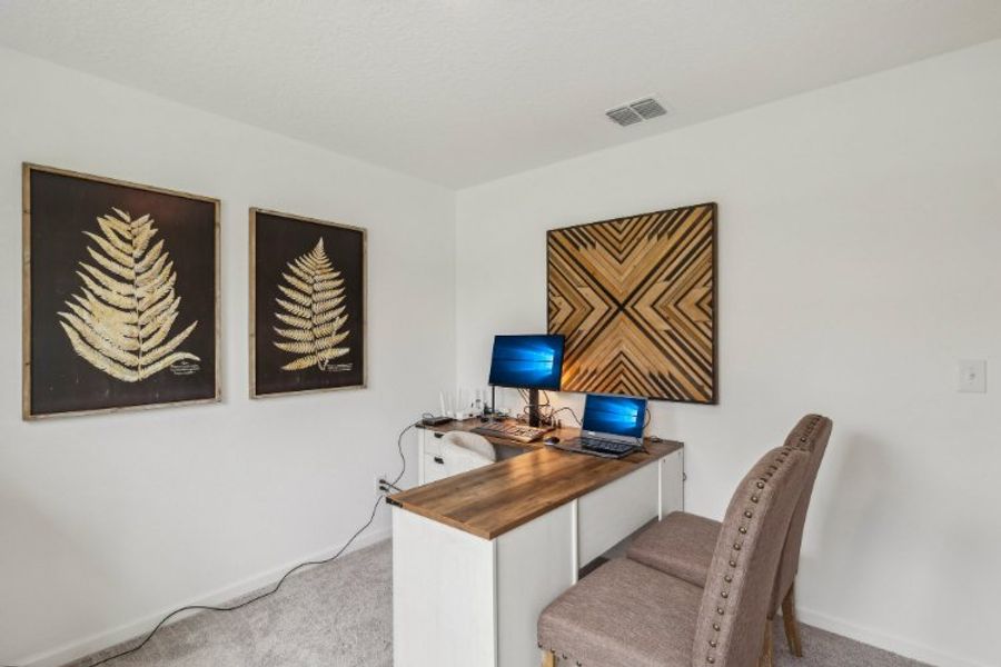 A desk with a computer and a chair in a room with pictures on the wall. A desk with a computer and a chair in a room with pictures on the wall.