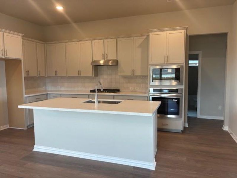 Kitchen featuring appliances with stainless steel finishes, dark wood-style flooring, a center island with sink, tasteful backsplash, and white cabinets Kitchen featuring appliances with stainless steel finishes, dark wood-style flooring, a center island with sink, tasteful backsplash, and white cabinets