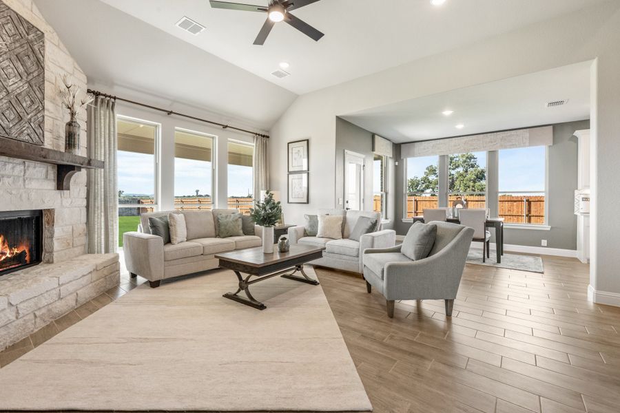 Open living room with stone fireplace, vaulted ceiling, ceiling fan, and large windows with backyard views