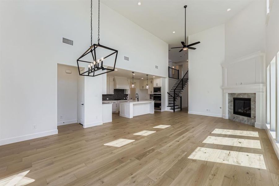 Unfurnished living room featuring a high ceiling, stairs, a fireplace, light wood-style floors, and a chandelier