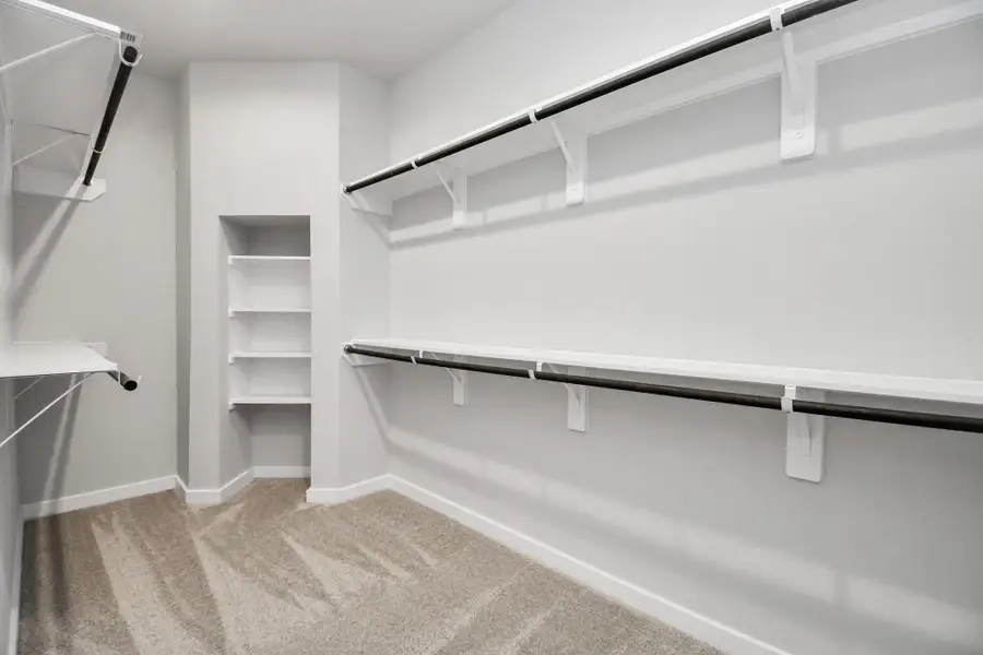 Discover luxury in this expansive walk-in closet, adorned with high ceilings and luxurious carpet. Sample photo of completed home with similar floor plan. Actual colors and selections may vary.