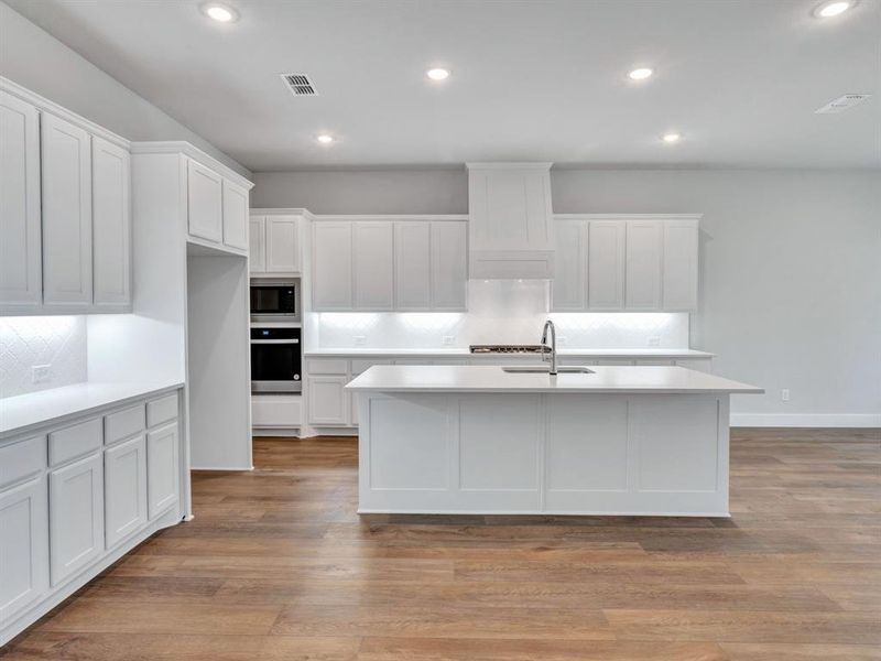 Kitchen with appliances with stainless steel finishes, tasteful backsplash, light hardwood / wood-style floors, and an island with sink