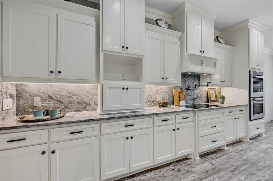 Kitchen with light stone counters, light hardwood / wood-style floors, white cabinetry, stainless steel double oven, and decorative backsplash