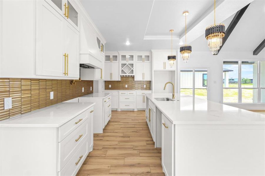 Kitchen featuring glass insert cabinets, white cabinets, a large island with sink, light wood-type flooring, and light stone countertops