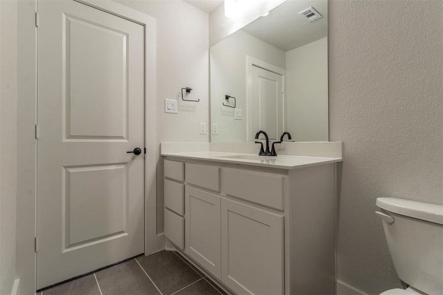 Half bath featuring a textured wall, vanity, and dark tile patterned flooring