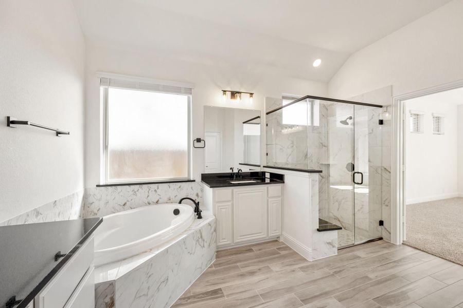 Master bathroom with marble soaking tub, glass walk-in shower, white vanity, and dark countertops on wood-look tile floors Master bathroom with marble soaking tub, glass walk-in shower, white vanity, and dark countertops on wood-look tile floors