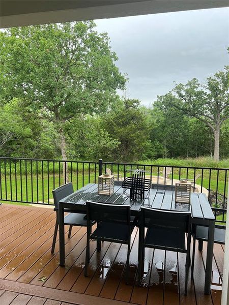Wooden terrace featuring outdoor dining space, a lawn, and view of wooded area