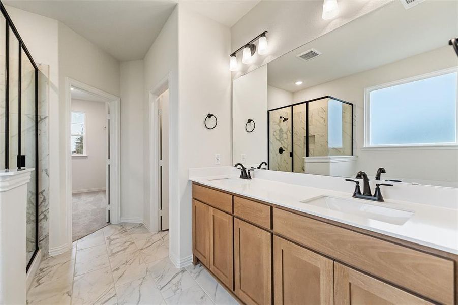 Bathroom featuring healthy amount of natural light, a marble finish shower, double vanity, and light marble finish flooring
