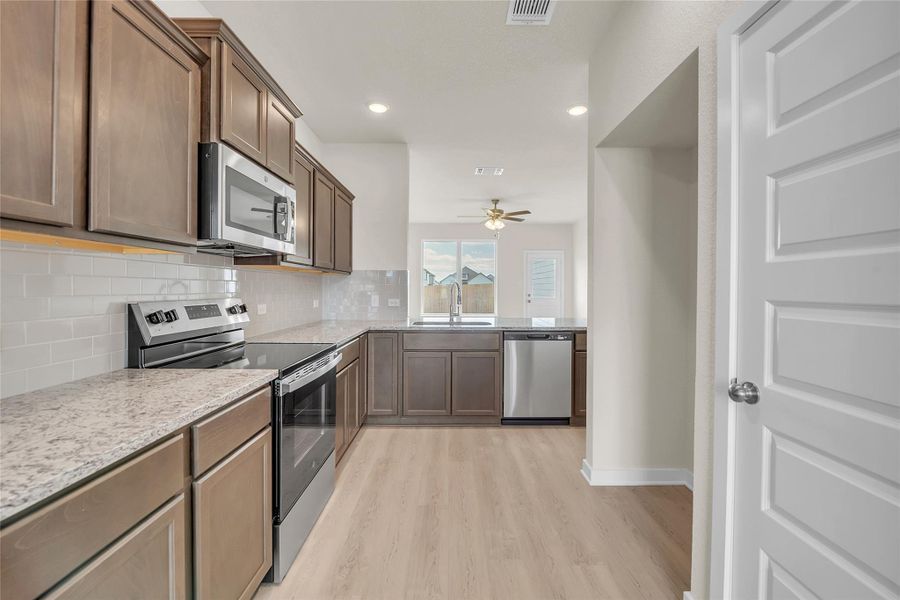 Kitchen featuring appliances with stainless steel finishes, recessed lighting, tasteful backsplash, light wood-style floors, and light stone countertops