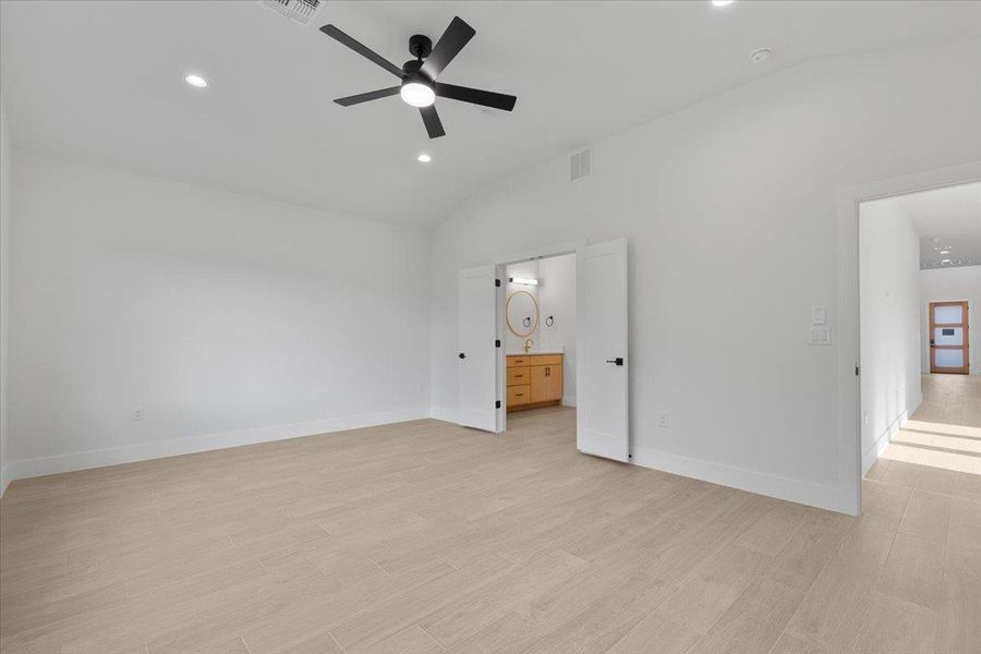 Unfurnished bedroom featuring light wood-type flooring, recessed lighting, lofted ceiling, ensuite bath, and a ceiling fan Unfurnished bedroom featuring light wood-type flooring, recessed lighting, lofted ceiling, ensuite bath, and a ceiling fan