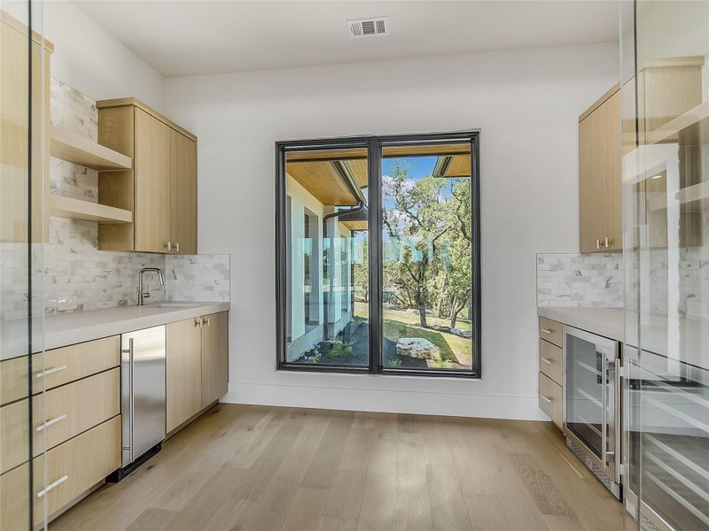 This space features light wood cabinetry, a white countertop, and a marble tile backsplash