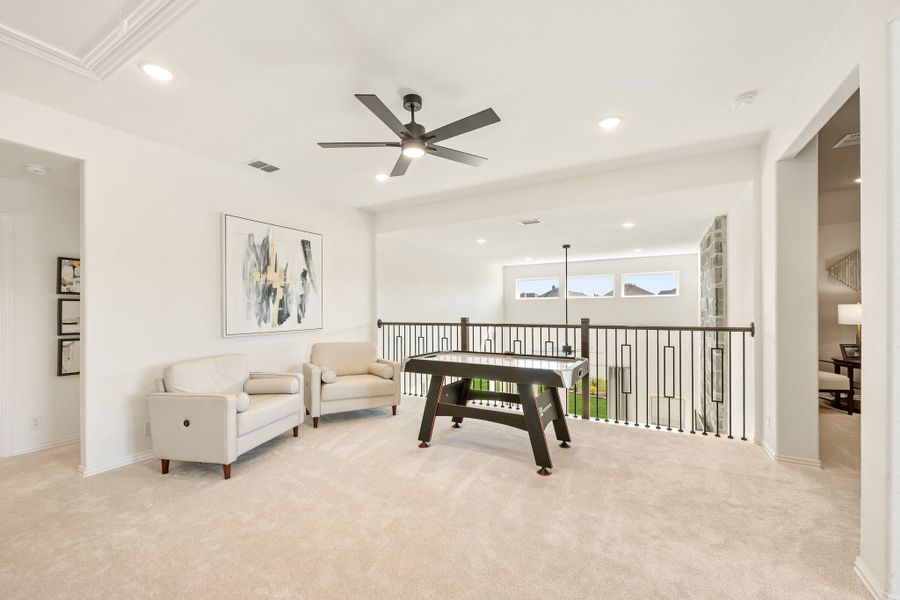 Upstairs loft game room with air hockey table, seating area, ceiling fan, and open iron railing overlooking lower level