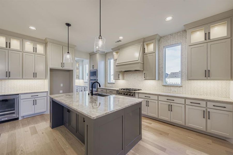 Kitchen with glass insert cabinets, light stone counters, wine cooler, premium range hood, and recessed lighting