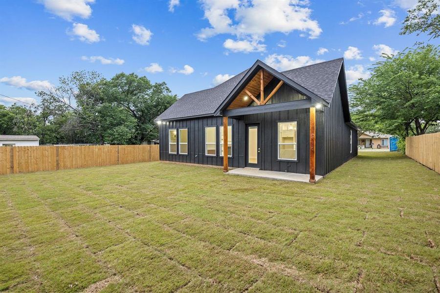 Modern farmhouse exterior featuring dark vertical siding, a covered patio with exposed wood beams and columns, and a new sod lawn Modern farmhouse exterior featuring dark vertical siding, a covered patio with exposed wood beams and columns, and a new sod lawn