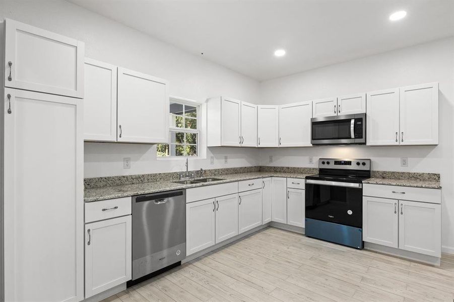 Kitchen with appliances with stainless steel finishes, white cabinets, light wood-style floors, light stone counters, and recessed lighting