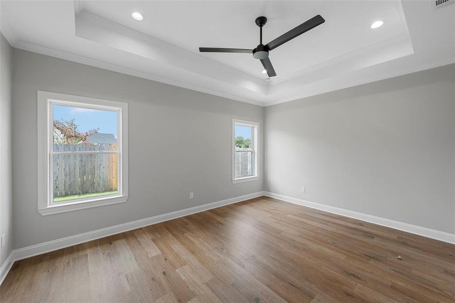 Empty room with a raised ceiling, light wood-style floors, crown molding, recessed lighting, and a ceiling fan Empty room with a raised ceiling, light wood-style floors, crown molding, recessed lighting, and a ceiling fan