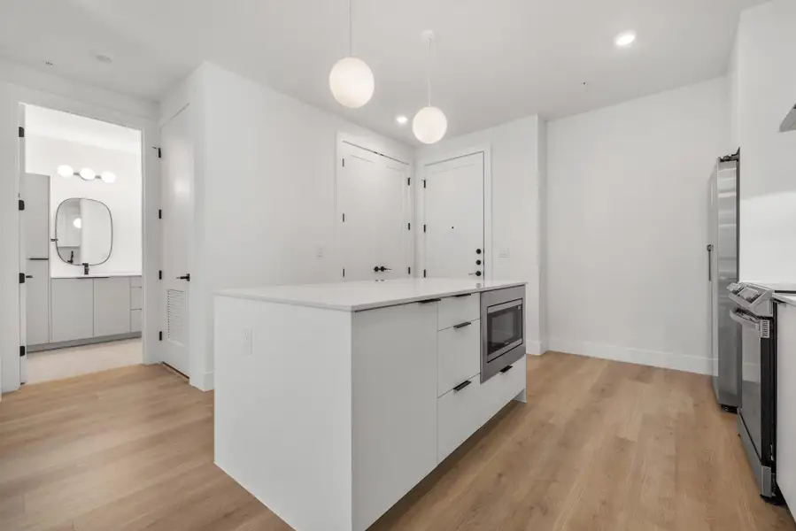 Kitchen featuring modern cabinets, white cabinetry, light wood-style floors, pendant lighting, and a kitchen island