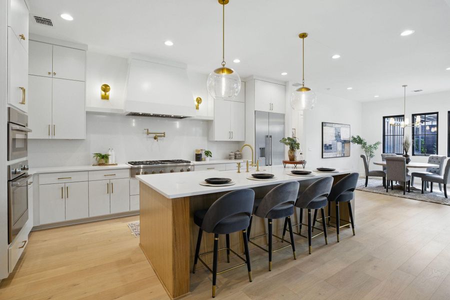 Kitchen featuring appliances with stainless steel finishes, premium range hood, light wood-style flooring, a center island with sink, and light countertops